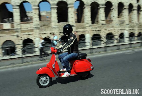 A red Vespa PX riding past the Colosseum in Rome.